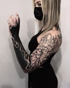 a woman wearing a black mask and holding her hands up to the side with tattoos on it