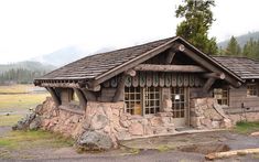 an old log cabin with stone walls and windows on the outside, surrounded by grass and trees