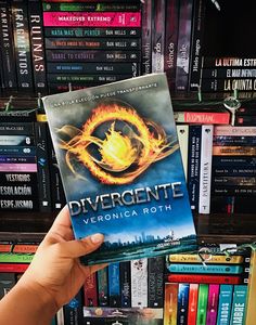 a person holding up a book in front of a shelf full of books and dvds