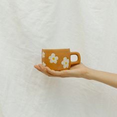 a hand holding a brown mug with white flowers on the outside and inside, in front of a white background