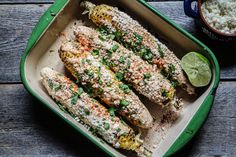 grilled corn on the cob in a green casserole dish with lime wedges