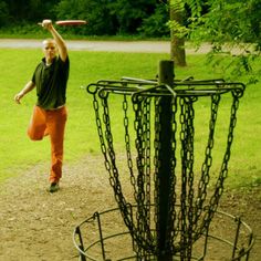 a man throwing a frisbee into a metal basket with chains on the ground