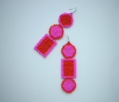 two pairs of pink and red beaded earrings on a white surface with one pair hanging from the back