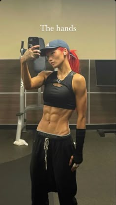 a woman taking a selfie in the gym with her cell phone and hat on