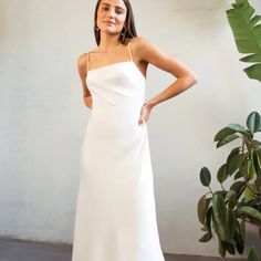 a woman standing in front of a plant wearing a white dress with one shoulder cut out