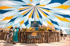 people are standing under a large umbrella on the beach with blue, yellow and white stripes