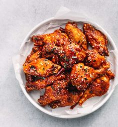 a white bowl filled with chicken wings covered in sesame seeds and seasoning on top of a gray surface