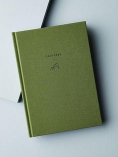 an open green book sitting on top of a white table next to a pair of scissors