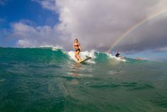 a person riding a surf board on a wave with a rainbow in the sky behind them