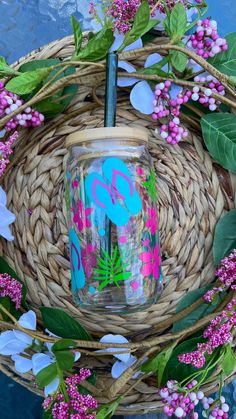 a close up of a glass on a table with flowers and leaves around it,