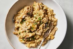 a white bowl filled with pasta and mushrooms on top of a marble countertop next to a fork