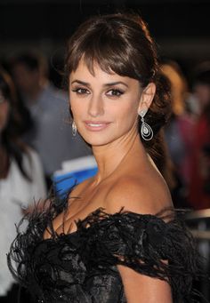 a woman in a black dress with feathers on her shoulder and earrings, posing for the camera