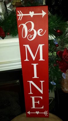 a wooden sign that says be mine on it next to a christmas tree in the background