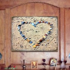 there is a heart made out of shells on the wall above a mantle with pictures and vases