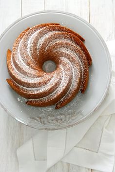 a bundt cake with powdered sugar on top sits in a bowl next to napkins