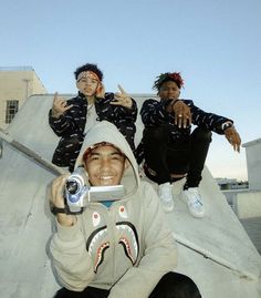 three young men sitting on top of a skateboard ramp with their hands in the air