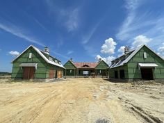 two large green barns sitting on top of a dirt road in front of a blue sky