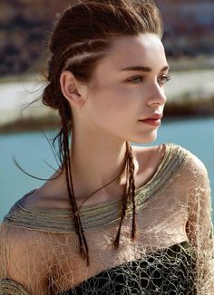 a woman with braids in her hair standing next to the water and looking off into the distance