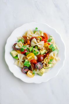 a white plate filled with pasta salad on top of a marble countertop next to a knife and fork