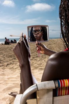 a woman sitting in a chair on the beach taking a selfie