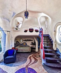 a living room with stairs leading up to the top floor and blue chairs in front of it