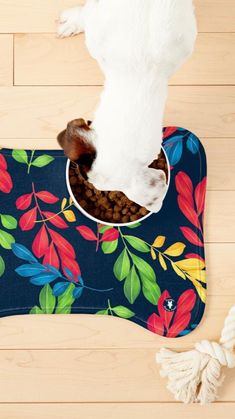 a dog eating out of a bowl on top of a mat with leaves and flowers