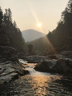 the sun shines brightly over some rocks and water in a river with trees on both sides