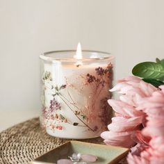 a pink flower next to a white candle on top of a wicker table cloth