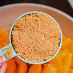 a person holding a spoon full of sugar over some carrots in a white bowl