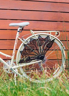 an old fashioned bicycle is parked in front of a wooden wall with grass and weeds