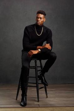 a man sitting on top of a stool wearing a black turtle neck sweater and pants