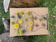 a piece of cardboard with flowers on it sitting in the grass next to a tree stump