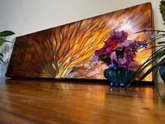 a vase filled with purple flowers sitting on top of a wooden floor next to a painting