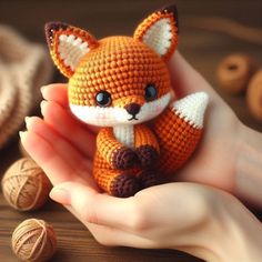 a hand holding a tiny crocheted fox on top of a table next to yarn balls