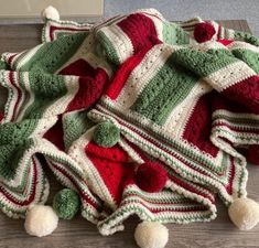 a crocheted blanket with pom - poms on the bottom is laying on top of a wooden floor