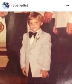 an old photo of a young boy in a tuxedo and bow tie standing next to other people