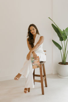 a woman sitting on top of a wooden stool next to a potted plant