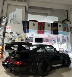 a black sports car parked inside of a garage next to other cars and posters on the wall