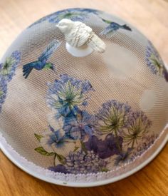 a blue and white flowered hat with a bird on the top, sitting on a wooden surface