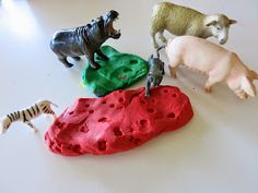 four toy animals on top of a white table next to some rocks and zebras