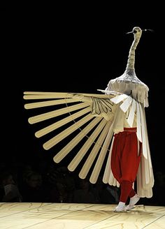 a woman is walking down the runway with an animal on her head and wings in front of her