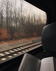 an open book sitting on top of a seat next to a train track with trees in the background