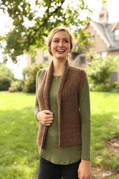 a woman standing in front of a tree wearing a brown knitted vest and smiling