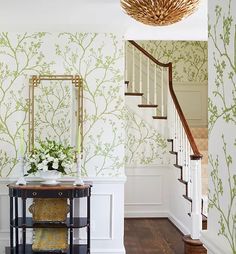 a foyer with green wallpaper and white walls, a mirror on the side table