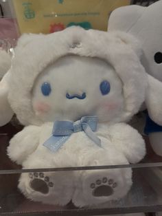 a white teddy bear with blue eyes and a bow on it's head sitting in a display case