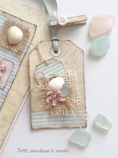 two tags with flowers on them sitting next to some sea glass beads and seashells