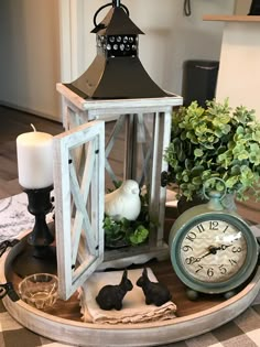 a clock and some plants on a table with a candle in the centerpiece next to it