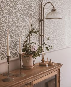 a wooden table topped with a vase filled with flowers next to a wall mounted light