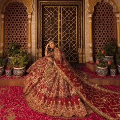 a woman in a red and gold bridal gown sitting on a bed of rose petals