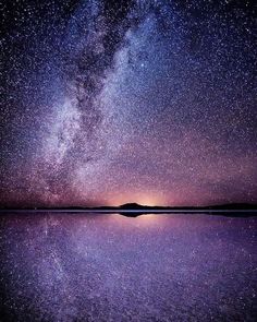 the night sky is filled with stars and reflecting in the water, while the milky shines brightly